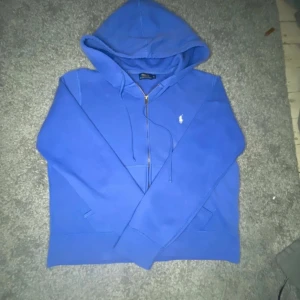 Blå hoodie från Ralph Lauren (XL barnstorlek) - Säljer en snygg blå hoodie från Ralph Lauren med dragkedja och klassisk logga på bröstet. Perfekt för en avslappnad stil. Den har en bekväm passform och huva med dragsko.