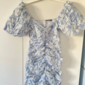 Sommar klänning  - Söt blommig klänning i ljusblått och vitt från Gina Tricot. Klänningen har puffiga kortärmar och en v-ringad hals. Den är rynkad längs med hela och ger en fin struktur när den är på. Perfekt för sommarens alla tillfällen! Midsommar eller sommarfest! 
