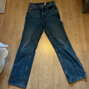 Blå jeansbyxor - Säljer ett par klassiska blå jeansbyxor med kåg midja och rak passform. Byxorna har fem fickor och stängs med dragkedja och knapp. Perfekta för en avslappnad stil.