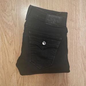 True religion jeans  - Snygga kolsvarta lågmidjade TR jeans med diamantknappar och klassisk femficksdesign. 34 cm midjemått. 