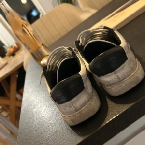 Vita oliver cabell - Säljer ett par vita sneakers med svart häl och en cirkeldetalj på sidan. Skorna har snörning och en klassisk design som passar till det mesta. Perfekta för en avslappnad stil.