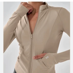 Beige träningsjacka  - Snygg beige träningsjacka från Ego med dragkedja framtill. Jackan har en tight passform och långa ärmar, perfekt för träning eller en aktiv vardag. Nyskick! Storlek 36 (liten i storleken!). 