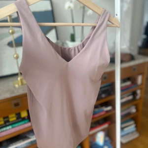 Träningstopp med inbyggd BH - Säljer en stilren beige/rosa träningslinne från Uniqlo. Toppen är ärmlös och tillverkad i ett mjukt och bekvämt syntetmaterial. Perfekt med inbyggd BH.