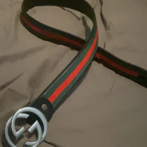 Randigt bälte med silverfärgat spänne - Snyggt bälte med ränder i grönt och rött samt ett stort, runt silverfärgat spänne. Perfekt för att ge en stilren touch till din outfit.