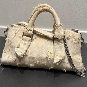 Beige axelväska med kedja - Säljer en skitsnygga beiga väska med slitna detaljer. Väskan har en kedja som axelrem och en dragkedja upptill. Säljer så den tyvärr inte kommer till användning längre💞pris kan diskuteras vid snabb affär