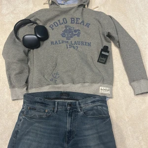 Grå hoodie från Ralph Lauren - Säljer en grå hoodie från Ralph Lauren med ett blått Polo Bear-tryck och texten '1967'. Tröjan har en klassisk huva med dragsko och ribbade muddar vid ärmslut och nederkant. Perfekt för en avslappnad stil. PRIS KAN DISKUTERAS 