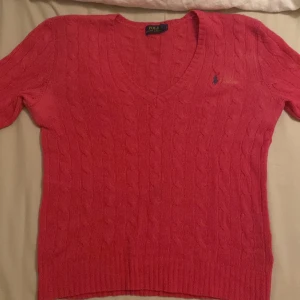 Rosa kabelstickad tröja från Ralph Lauren - Säljer en snygg rosa stickad tröja från  Ralph Lauren med kabelstickat mönster och v-ringning. Tröjan har långa ärmar och den klassiska loggan broderad på bröstet. Mestadels i merinoull och egentligen väldigt dyr men har använts en del därav fläckarna. Pris är diskutabelt.