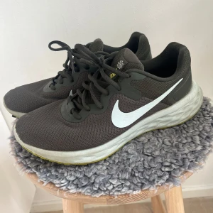 Nike sneakers - Säljer ett par svarta Nike sneakers med vit sula och klassisk snörning. Skorna har en gul detalj på sulan och är perfekta för träning eller vardagsbruk. De har en stilren design med Nike-loggan i vitt på sidan.