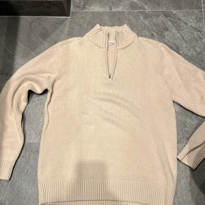 Beige tröja med dragkedja från dobber - Säljer en stilren beige tröja med dragkedja och ribbade detaljer vid ärmslut och nederkant. Perfekt för en avslappnad look. 