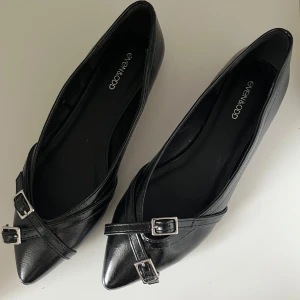 Svarta ballerinaskor med spänne - Eleganta svarta ballerinaskor från Even&Odd med spetsig tå och dekorativa spännen. Perfekta för en stilren look.