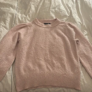 Ljusrosa stickad tröja med puffärm - Supermysig ljusrosa stickad tröja med puffiga axlar och rund halsringning. Tröjan har en mjuk och fluffig känsla, perfekt för att hålla sig varm under kyliga dagar. Långärmad och med ribbade muddar vid ärmslut och nederkant.