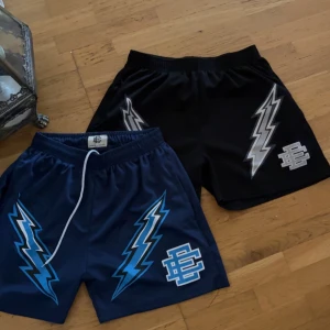Svarta & marinblå Eric emanuel - (200kr för en 350 för Båda). Två par shorts från EE, passar bra för S. ett par svarta med silverfärgade blixtar och ett par marinblå med blå blixtar. Båda har elastisk midja och dragsko, samt en stor logga framtill. Perfekta för sport eller chill.