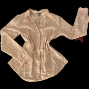Ljusrosa randig skjorta från H&M - Snygg ljusrosa skjorta från H&M i storlek 42. Skjortan har tunna vita ränder, klassisk krage och knäppning framtill. Tillverkad i mjuk bomull och har långa ärmar med manschett. Perfekt för en chill och stilren look.