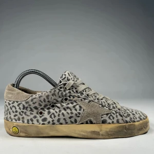 Leopardmönstrade golden goose - Grå sneakers från Golden Goose med leopardmönster, beige mockadetaljer och ikonisk stjärna på sidan. Skorna har snörning, rund tå och en gulnad sula med smiley-detalj på hälen. Perfekt för dig som gillar en edgy och trendig look.