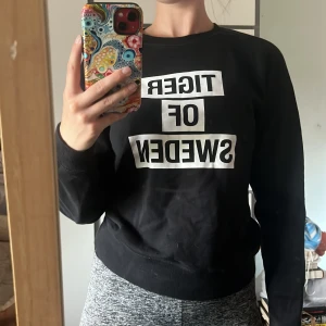Svart sweatshirt Tiger of Sweden XS - Svart sweatshirt från Tiger of Sweden i storlek XS. Tröjan har vit text framtill, rund halsringning och långa ärmar. Mjuk bomullskänsla och ribbade muddar vid ärmslut och nederkant. Perfekt för en chill och stilren look. Använd fåtal gånger! 
