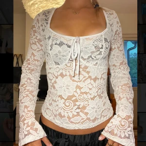 Vit spetsblus med knyt och blommönster -  Vit blus i ganska genomskinlig spets med blommor och snygg knytning framtill. Långärmad och figurnära passform med fyrkantig urringning. Är mycket bra skick utan defekter, endast använd en gång!