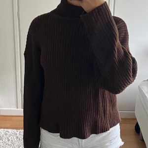 Brun ribbstickad polotröja - Mysig kaffebrun polotröja med ribbad struktur och lång ärm. Tröjan har en hög krage och är stickad i ett mjukt material, perfekt för kyligare dagar. Passformen är lite loose och ger en avslappnad vibe.