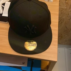 Svart New Era 59FIFTY Yankees keps - Snygg svart New Era 59FIFTY keps med New York Yankees-logga ton-i-ton framtill. Klassisk flat peak och broderad MLB-logga bak. Kepsen är i bomull och har en stilren, urban look som passar perfekt till streetwear. Pris går att diskutera 
