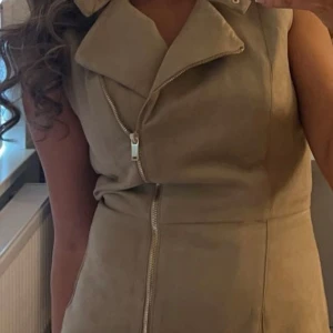 Beige mockaklänning med dragkedja - Snygg beige klänning i mocka-look med markerad krage och dragkedja framtill. 