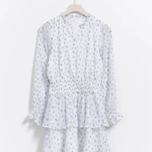 Blommig volangklänning Gina Tricot - Slutssåld supersöt kort volangklänning från Gina Tricot i vitt med blått blommönster som bara har använts 1 gång! Perfekt för dig som gillar något luftigt och som vill vara extra fin vid ett speciellt tillfälle.