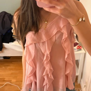 Rosa volang topp med oneshoulder - Säljer en superfin rosa topp med volanger och oneshoulder-design. Toppen är ärmlös och har en luftig känsla, perfekt för varmare dagar. Materialet är lätt och ger ett snyggt fall. Passar dig som gillar romantisk och trendig stil.