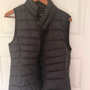 Svart dunväst från Only - Snygg svart dunväst från Only med quiltad design och hög krage. Västen har dragkedja framtill och är perfekt att slänga över en hoodie eller tröja för extra värme. Enkel och stilren look som funkar till det mesta.