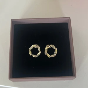 Guldiga örhängen med stenar - Snygga runda örhängen i guld med tvinnad design och glittrande stenar. Perfekta för att ge din look lite extra bling.