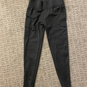 Svarta leggings från Newbody med ficka - Svarta leggings från Newbody och praktisk sidoficka. Tight passform och stretchigt material som passar perfekt till träning eller chill. Snygg och enkel design som är lätt att matcha med andra plagg.