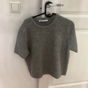 Grå stickad kortärmad tröja Zara - Mysig grå stickad tröja från Zara i storlek L. Tröjan har korta ärmar, rund halsringning och ribbade kanter. Perfekt för lager-på-lager och funkar året runt när du vill ha en chill men ändå stilren look. Är storlek L men skulle mer säga att den passar som M