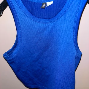 Blå ribbad linnetopp från Divided - Säljer en blå ribbad linnetopp från Divided. Toppen är croppad och ärmlös med rund halsringning och stretchigt material. Perfekt att styla med jeans eller kjol för en cool och enkel look.