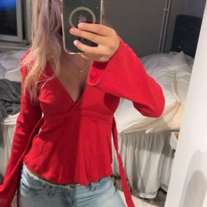 Röd omlottopp med v-ringning - Säljer en röd omlottopp med djup v-ringning och långa, vida ärmar.  Har endast använt på julafton säljer en likadan i rosa