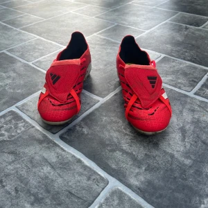 Adidas Predator röda fotbollsskor  - Säljer ett par röda Adidas Predator fotbollsskor med vita och svarta detaljer. Skorna har snörning, täckt plös och klassisk Predator-design med mönstrad ovandel. Använda 5 gånger 