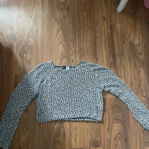 Svartvit croppad stickad tröja DIVIDED - Säljer en croppad stickad tröja från DIVIDED i svart och vitt. Tröjan har lång ärm och ett coolt, bubbligt mönster som ger en unik textur. Perfekt för dig som gillar trendiga och bekväma plagg med lite edge.