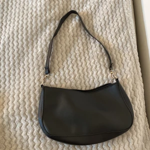 Svart axelväska i skinnimitation - Enkel och stilren svart axelväska med mjukt rundad form och justerbart axelband. ❤️