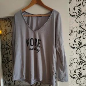 Grå långärmad tröja med tryck - Ljusgrå långärmad tröja med v-ringning och svart texttryck på bröstet där det står 'NOPE. not today'. Skön och avslappnad passform, perfekt för chill dagar. Tillverkad i mjuk bomull som känns bekväm mot huden.
