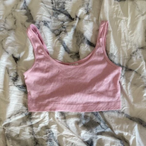 Rosa ribbad linnetopp från H&M Divided - Säljer en ljusrosa ribbad linnetopp från H&M Divided. Toppen är croppad med breda axelband och har en enkel, stilren design som passar perfekt till jeans eller kjol. Gjord i mjuk bomull för en bekväm känsla hela dagen.