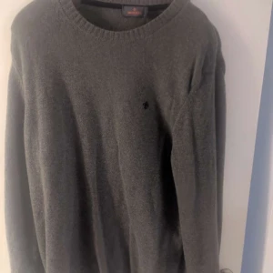 Grå stickad tröja från Morris XL - Mysig grå stickad tröja från Morris i storlek XL. Klassisk rund halsringning och diskret broderad logga på bröstet. Perfekt för lager-på-lager och passar till både jeans och chinos. Materialet är mjukt och värmande ull.