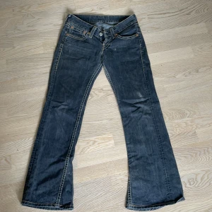 Lågmidjade Levis jeans  - Dessa jeans sitter för tajt för mig då det är därför jag säljer dem, taggen på baksidan är trasig men det är inte så att det påverkar något. Jeansen är ungefär 3cm ovanför hälen på mig som är 173cm.  Midjemått- 38cm    Lår-27cm tvärsöver där det är som tjockast. Finns inga ställen förutom taggen som är trasig. Jeansen är bootcut/flare. Färgen är mörkblå/mörkgrå.