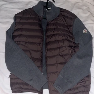  Cardigan från Moncler med grå ärmar - Cardigan från Moncler med quiltad front och grå stickade ärmar. Är i helt nytt skick endast andvänd en gång.storleken på den är L men den sitter som en M .Priset kan diskuteras vid snabb affär 