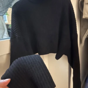 Svart croppad stickad tröja Zara - Svart ribbstickad croppad tröja från Zara med lång ärm och hög hals. Tröjan har en loose passform och är perfekt för lager-på-lager. Materialet är mjukt och ger en chill vibe till outfiten.