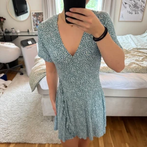 Blommig omlottklänning Pull&Bear - Supersöt kort omlottklänning från Pull&Bear i grönt med vitt blommönster. Klänningen har v-ringning, knyt i sidan och korta ärmar.😇