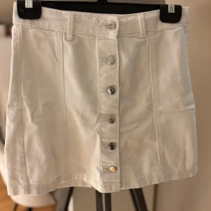 Vit jeanskjol med knappar från g perfect jeans - Vit kort jeanskjol från g perfect jeans i storlek 36. Kjolen har raka sömmar, bälteshällor och snygga silverfärgade knappar framtill. Perfekt för dig som gillar en clean och stilren look.