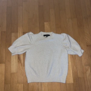 Ljusbeige stickad tröja med puffärm - Superfin ljusbeige stickad tröja från Vero Moda med korta puffärmar och rund hals. Tröjan har ribbade muddar och en mjuk, mysig känsla. Perfekt för lager-på-lager och enkel att styla med jeans eller kjol.