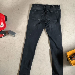 Svarta jeans från Dolce & Gabbana - Snygga svarta jeans från Dolce & Gabbana med diskreta slitningar och klassisk femficksdesign. Byxorna har DG-logga i metall bak och är tillverkade i bomull med lite stretch för skön passform. Perfekta för dig som gillar stilrena och exklusiva jeans.