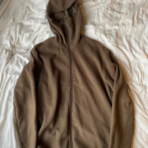 Brun fleecejacka från Weekday - Säljer en brun fleecejacka med balaklava hood från Weekday i storlek XL. Den har ett litet brännmärke framtill, men knappt något som syns!