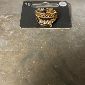 Guldiga ringar med stenar - Säljer ett set med guldiga ringar, varav en är dekorerad med glittrande stenar. Perfekt för att lägga till lite bling till din outfit. Passar bra att bära tillsammans eller var för sig.