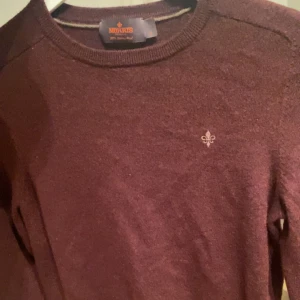 Vinröd tröja från Morris - Säljer en stilren vinröd tröja från Morris i 100% merinoull. Tröjan har en liten broderad detalj på bröstet och rund halsringning. Perfekt för kyligare dagar. Original storlek S men den har krympt i tvätten så storleken nu är ungefär xxs/xs. Priset kan diskuteras.
