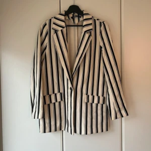 Randig kavaj i svart och vit - Snygg randig kavaj i svart och vit med klassisk krage och knäppning fram. Perfekt för en stilren look. Långärmad design med fickdetaljer på sidorna.