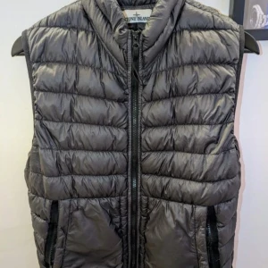 Grå/svart Stone Island dunväst  - Grå/svart dunväst från Stone Island med dragkedja två större fickor framtill och hög krage. Storlek S, normal i storleken. Inga synliga defekter. Skickar gärna fler bilder på förfrågan