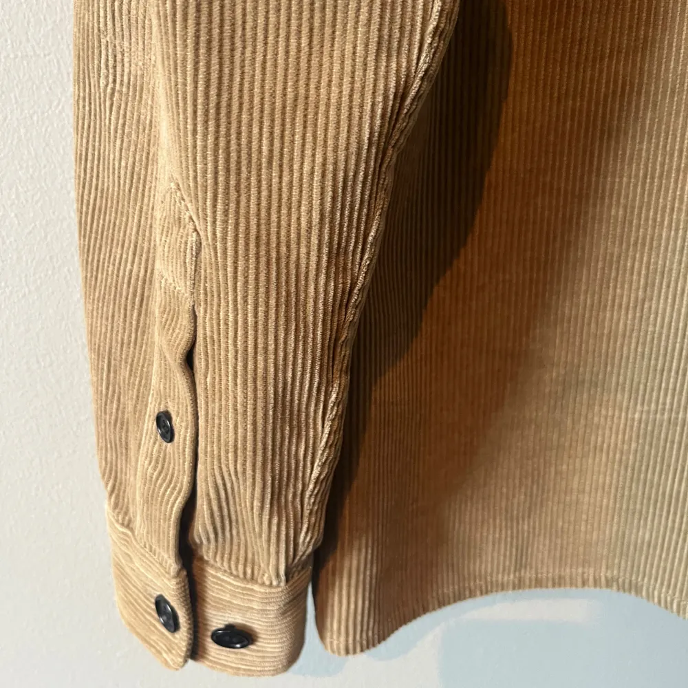 Säljer en snygg beige manchester overshirt med knappar framtill. Den har en regular fit och två praktiska bröstfickor. Perfekt för lager-på-lager-stilen under höst och vår. Långärmad design med en stilren look.. Takit.